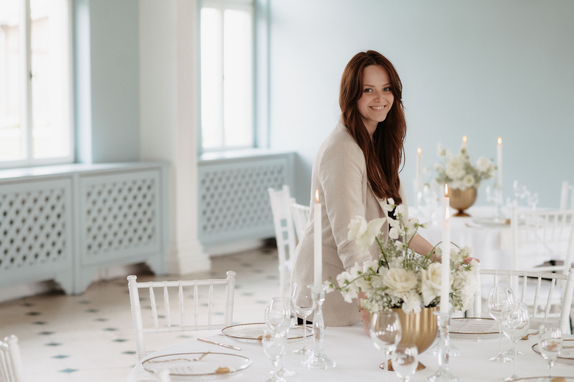 Hochzeitsplanerin Romina Blume überprüft lachend weiße und goldene Tischdekoration und führt letzte Handgriffe aus.