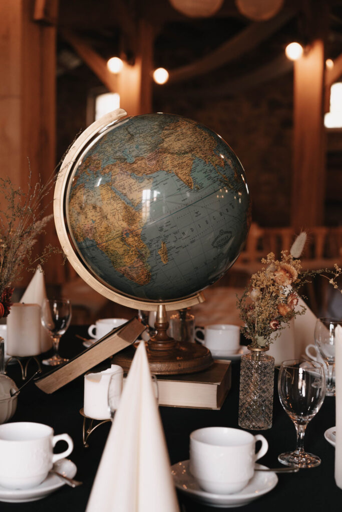 Detailaufnahme einer Tischdekoration mit antikem Globus, Trockenblumen und Bücherstapel bei einer Scheunenhochzeit und Landhochzeit in Berlin und Brandenburg.