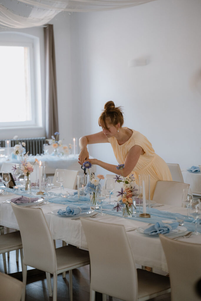 Hochzeitsplanerin Romina Blume richtet eine festlich gedeckte Tafel mit hellblauen Servietten und Blumen am Haus am Bauernsee her.