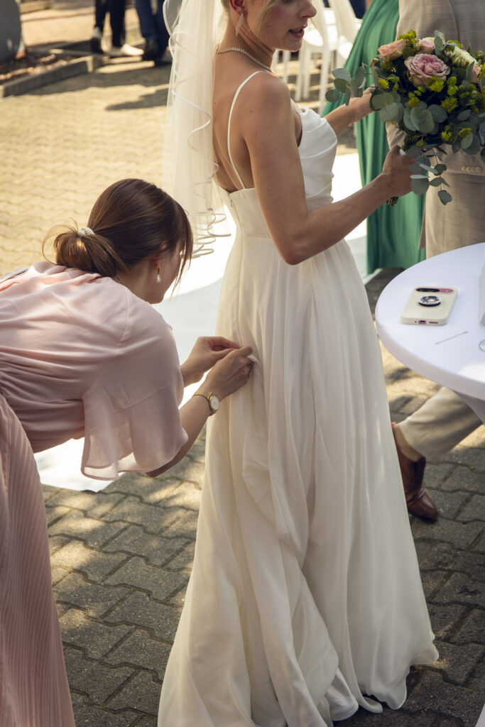 Hochzeitsplanerin Romina Blume richtet das Brautkleid einer Braut während der Hochzeitsfeier.